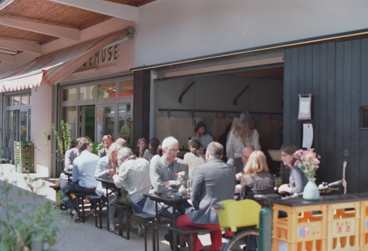 Gäste sitzen im Außenbereich eines modernen Restaurants an Tischen und Bänken.